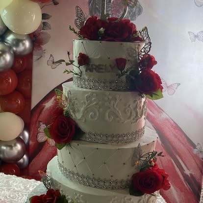 Pastel de quinceañera de varios pisos en blanco, decorado con rosas rojas, detalles plateados y mariposas.